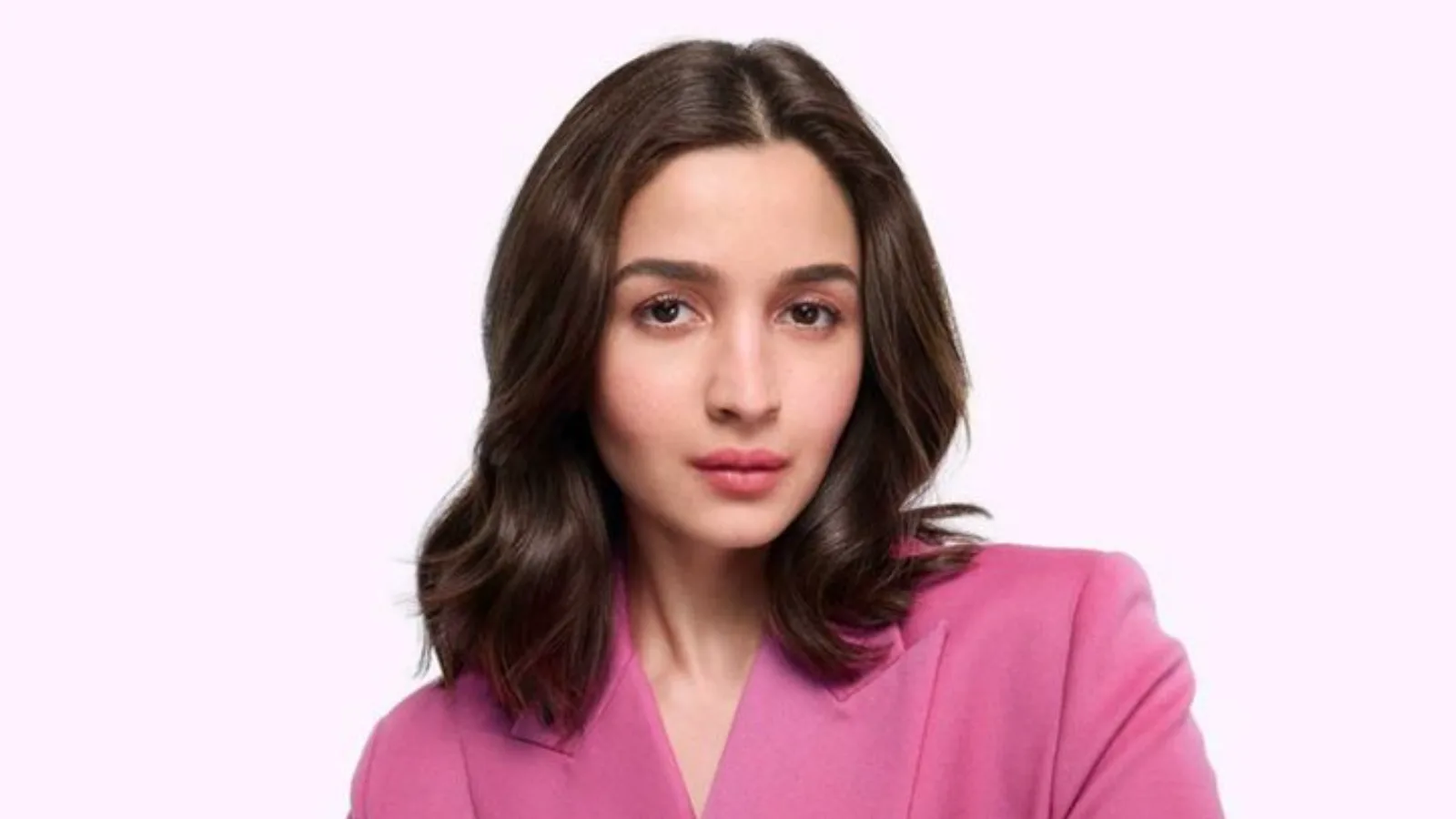Alia Bhatt, a young Indian woman with dark wavy hair, wearing a bright pink blazer, looking directly at the camera with a calm expression against a light pink background.
