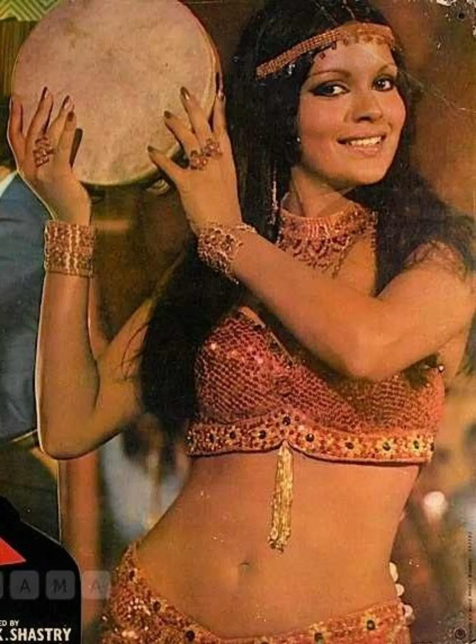 Zeenat Aman performing a dance with a tambourine, wearing a sparkling outfit and jewelry.