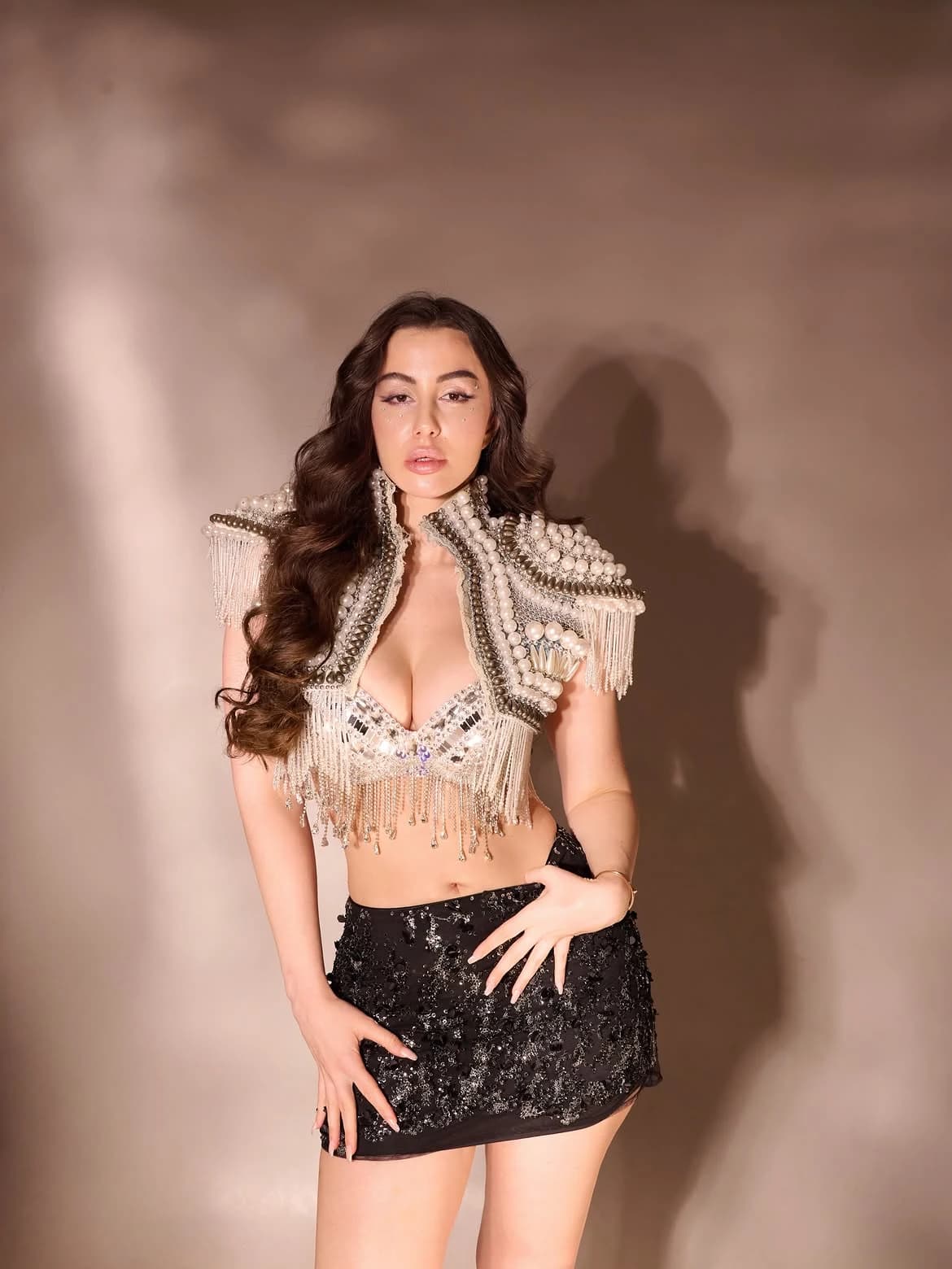 Giorgia Andriani posing confidently in a pearl and sequin embellished bolero jacket, matching bralette, and a black sequined mini-skirt, with long wavy hair.