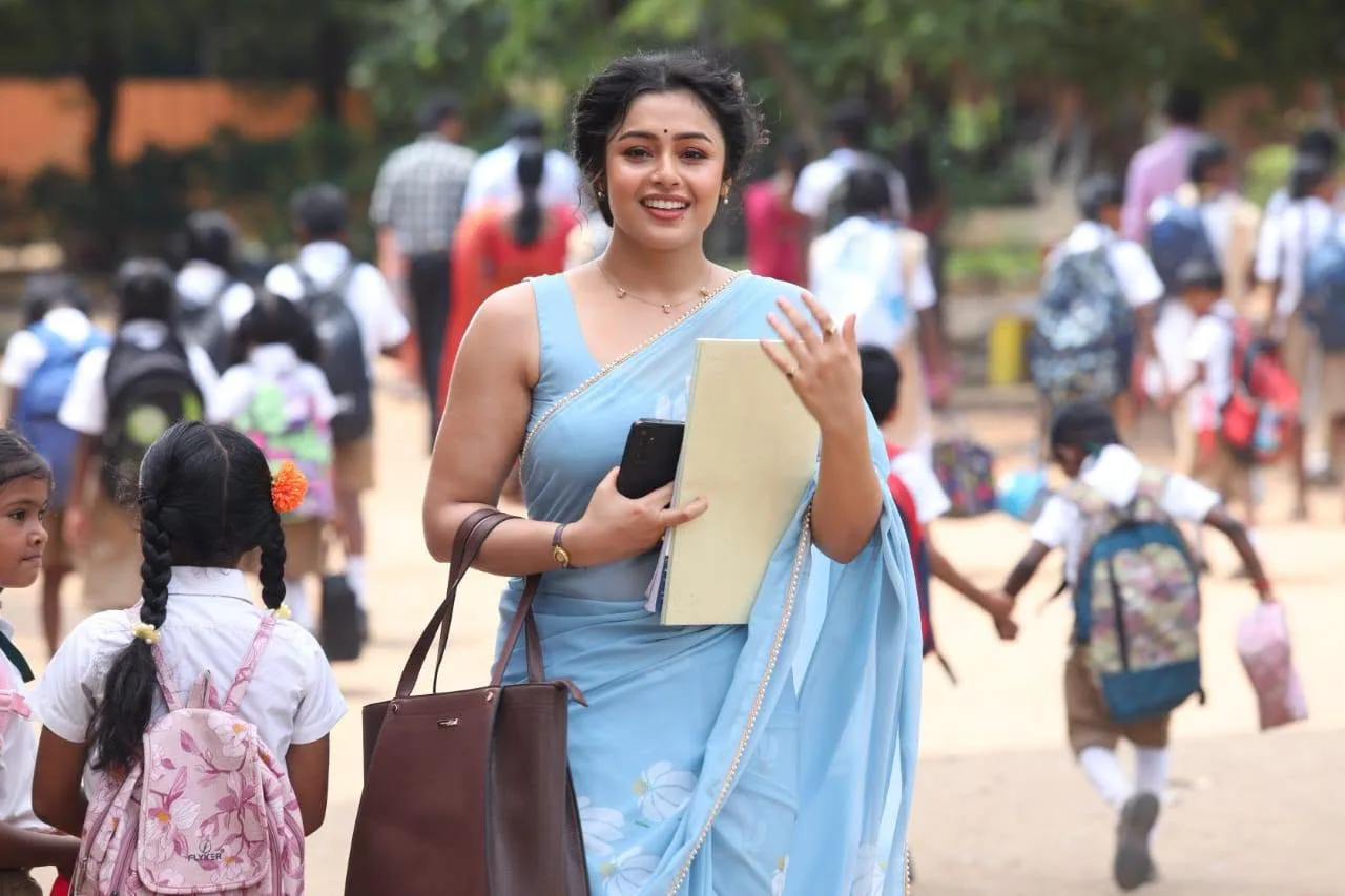Mokksha smiling in a light blue sleeveless saree holding a folder in a schoolyard scene from Gatta Kusthi 2.