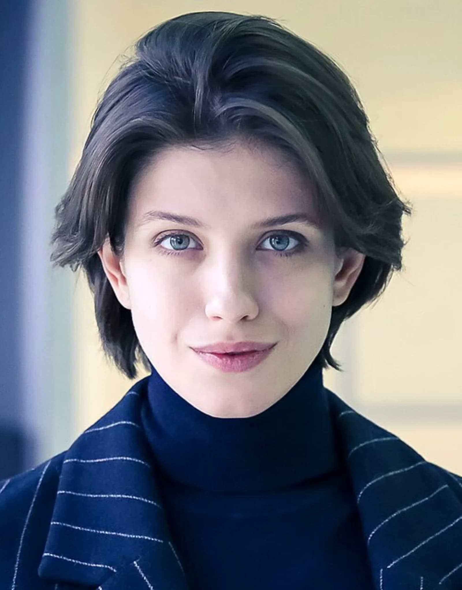 Close-up portrait of Russian actress Anna Chipovskaya with short hair and blue eyes wearing a navy turtleneck and pinstripe jacket.