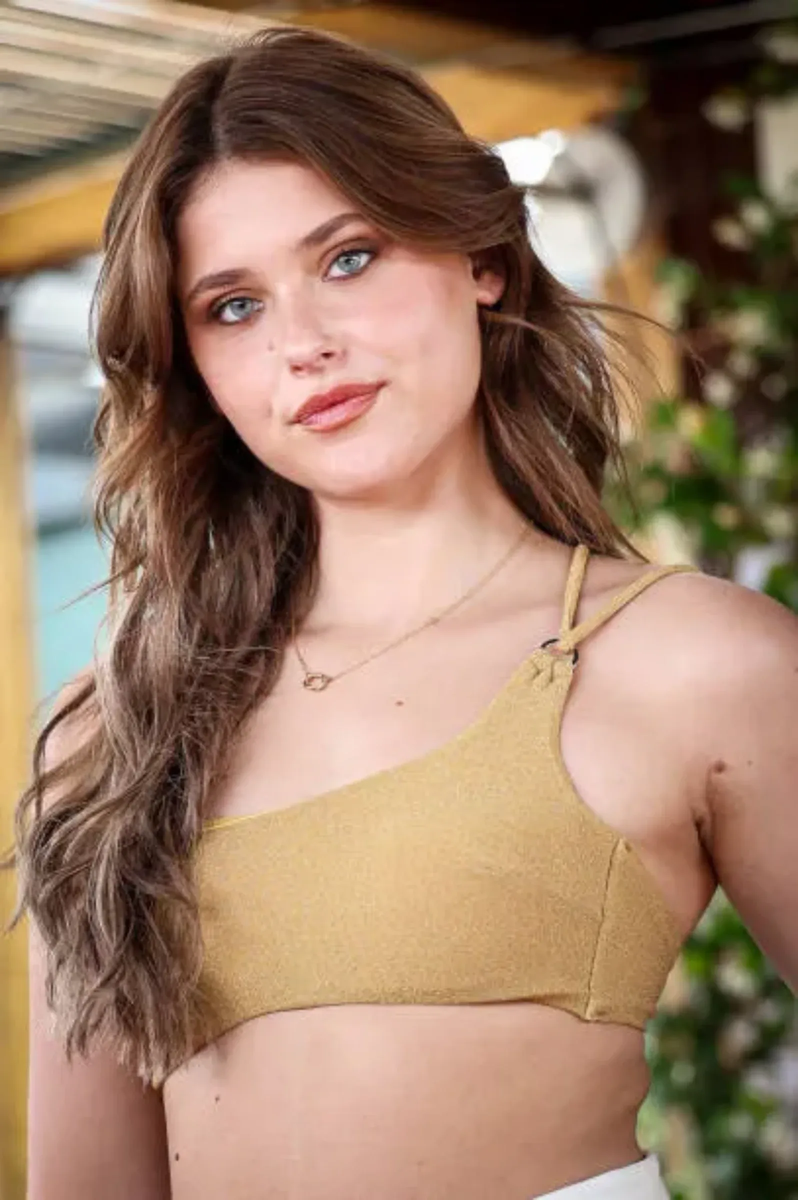 Nicole Wallace posing outdoors wearing a shimmering golden top, highlighting her stunning features and stylish appearance.