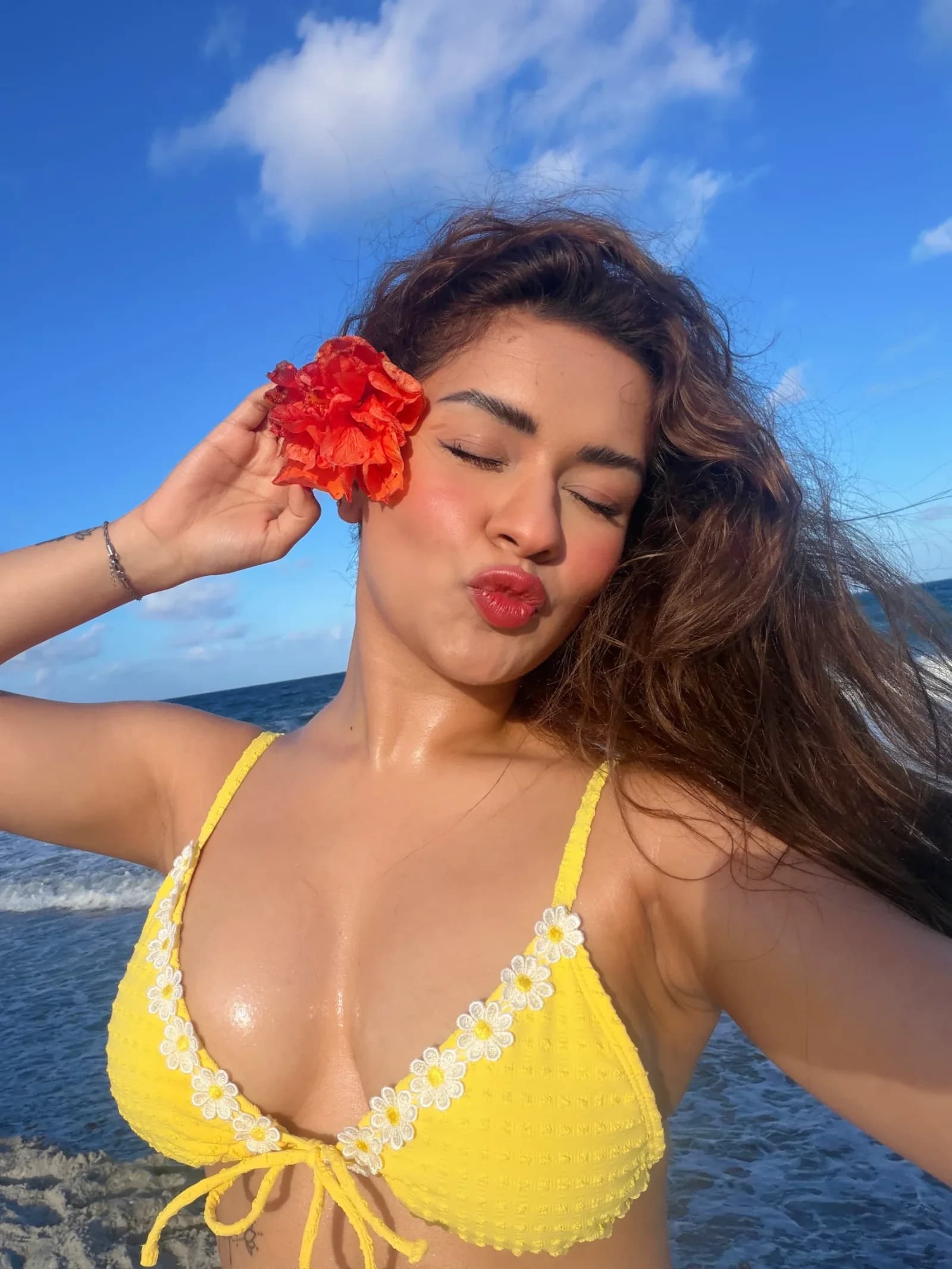 Avneet Kaur pouting in a yellow bikini top with a red flower behind her ear at the beach